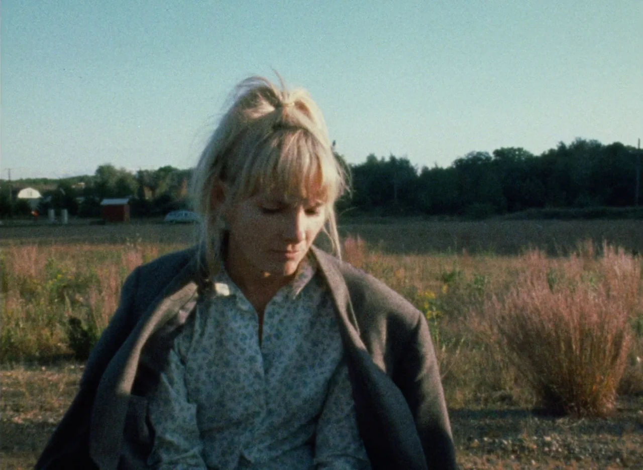 Wanda (1970) movie still: medium — A woman stands in a dry, grassy field during the late afternoon. She looks down while wearing a grey blazer over…