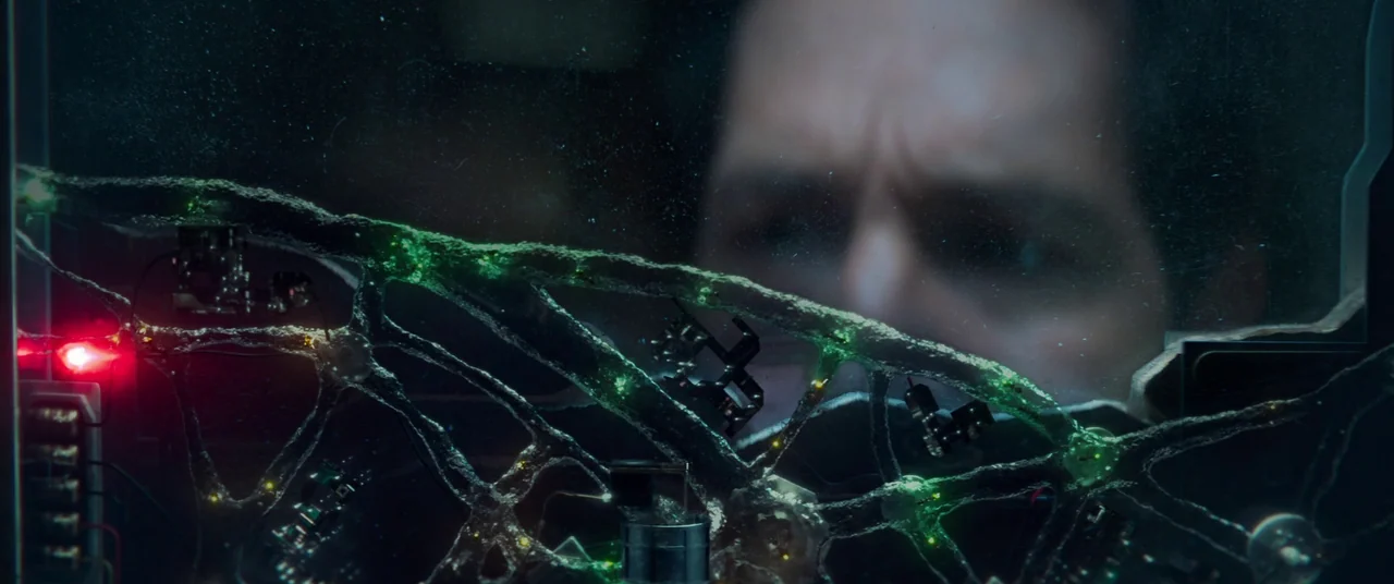 Ant-Man and the Wasp: Quantumania (2023) movie still: closeup — A dark laboratory features a glass partition displaying an intricate, glowing green…