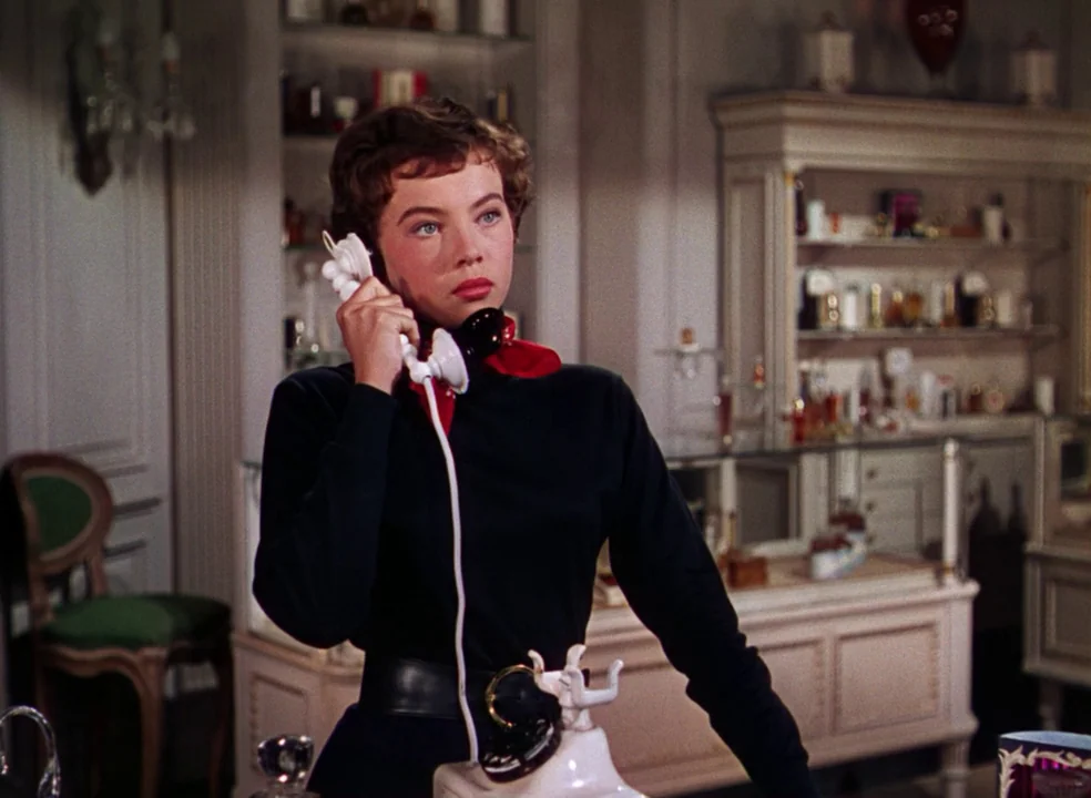 An American In Paris (1951) movie still: medium — An interior retail store features display cabinets stocked with glass perfume bottles. A young…