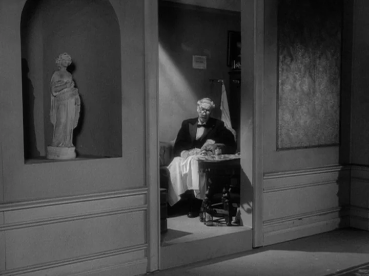 The Silence (1963) movie still: medium — A dark, formal sitting room contains a wall niche featuring a classical female statue. A man in formal wear…