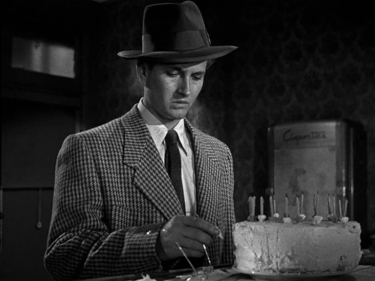 The Big Night (1951) movie still: medium — A dimly lit room with patterned wallpaper features a young man in a fedora. He carefully lights candles…