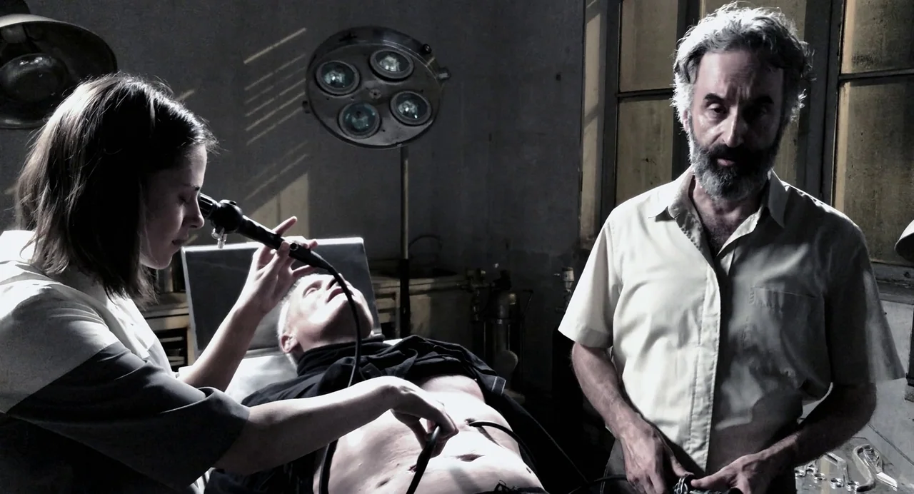 Crimes of the Future (2022) movie still: medium — A dimly lit, vintage surgical room features a patient on a metal table. A female doctor performs a…
