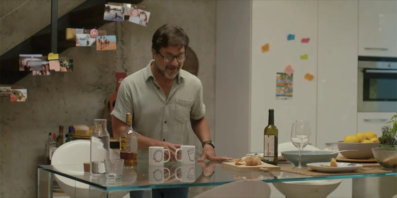 Instant Love (2020) movie still: medium — A modern home dining area features concrete walls decorated with small polaroid photographs. A man in a…