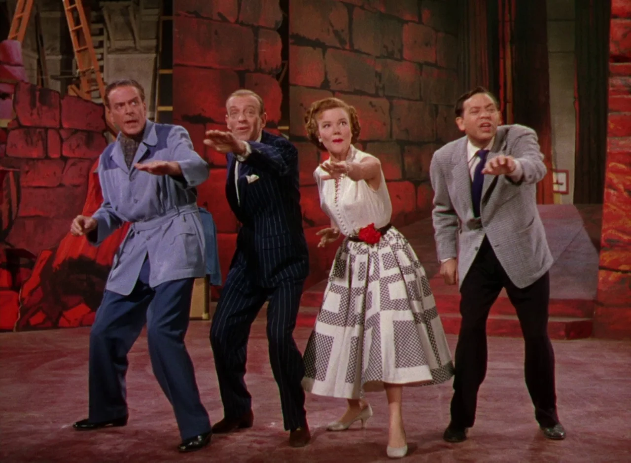 The Band Wagon (1953) movie still: fullbody — A brightly lit soundstage featuring a faux-stone wall painted in deep red and orange. Four people in…