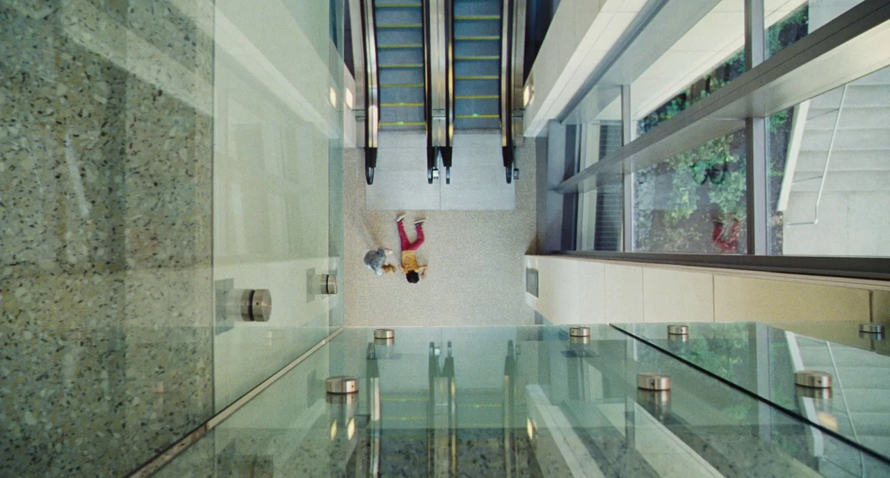The Killing of a Sacred Deer (2017) movie still: wide — A modern glass and concrete atrium features escalators and large glass wall panels. Two…