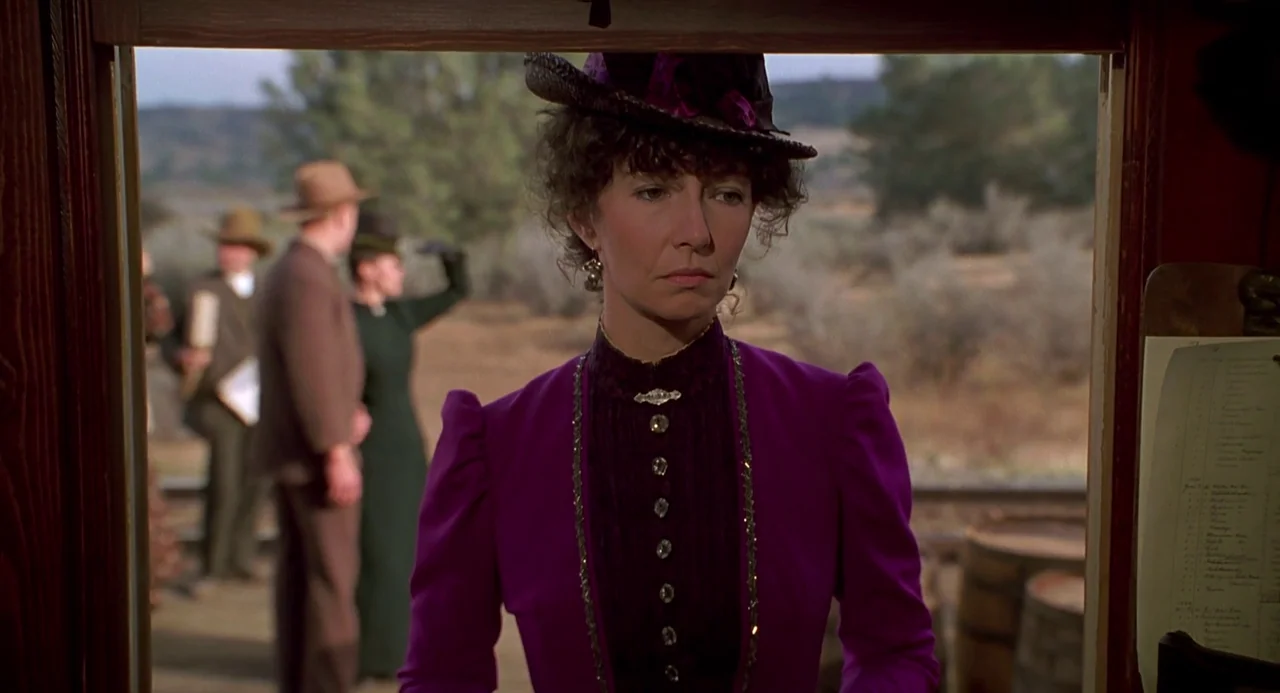 Back To The Future Part III (1990) movie still: medium — A woman stands in a wooden doorway of a train station platform. Behind her, other people in…