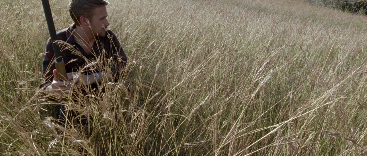Song to Song (2017) movie still: medium — A man kneels within a dense expanse of dried, golden-brown grasses in a meadow. He maintains a low profile…