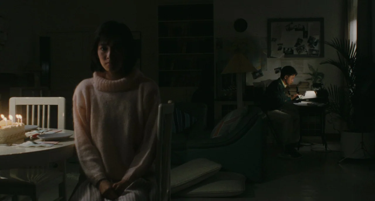 A Better Tomorrow (1986) movie still: medium — A dark living room contains a woman sitting at a table with candles. A man sits further back at a…