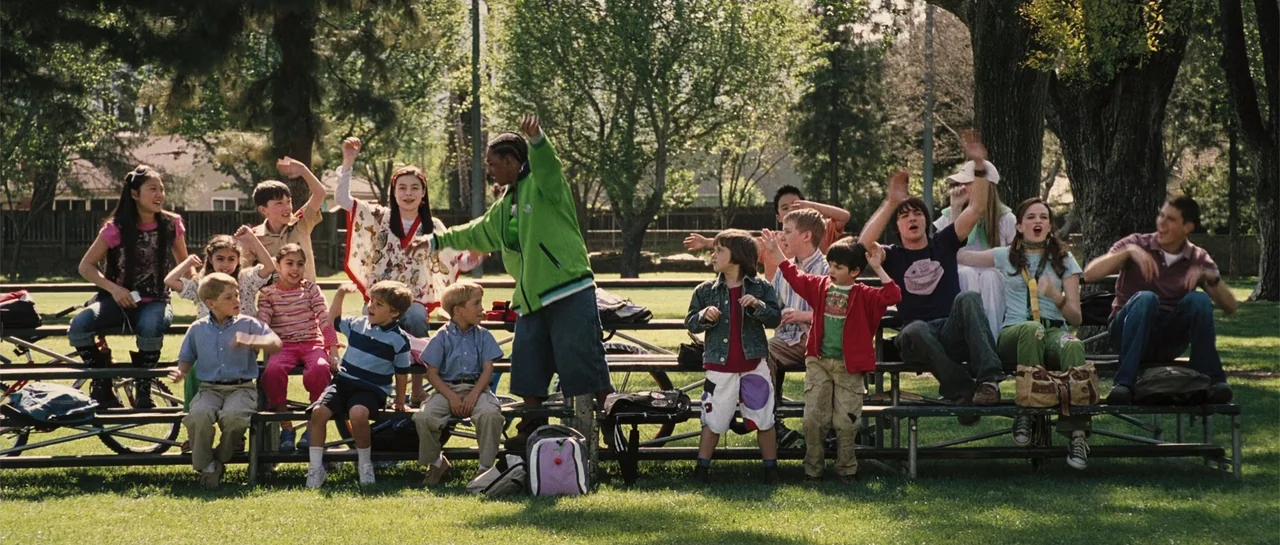 Yours, Mine & Ours (2005) movie still: wide — A group of diverse children sit on metal bleachers in a sunny park setting. They are cheering and…