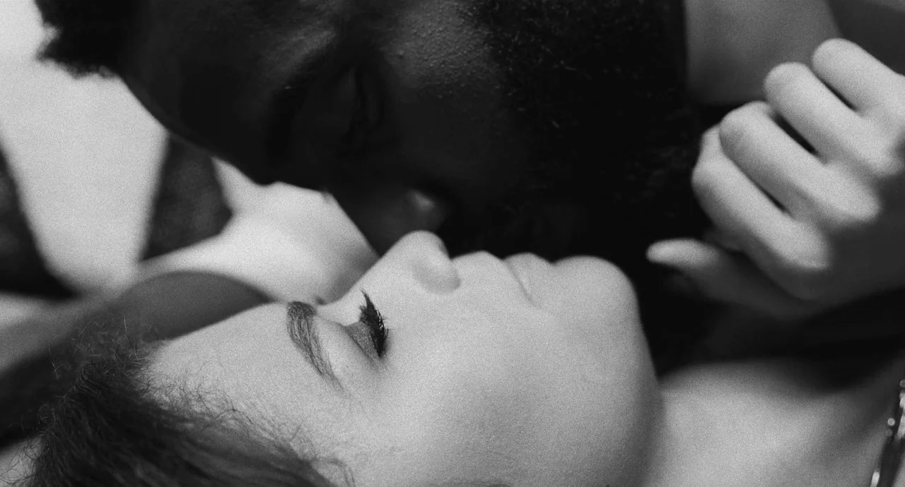 Malcolm & Marie (2021) movie still: closeup — A close perspective focuses on the heads of two individuals lying on a bed. The man leans over the…