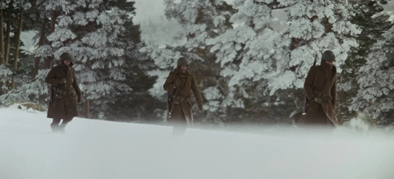 Patton (1970) movie still: fullbody — Three soldiers walk across a snow-covered hill flanked by tall snow-dusted evergreen trees. The men move…