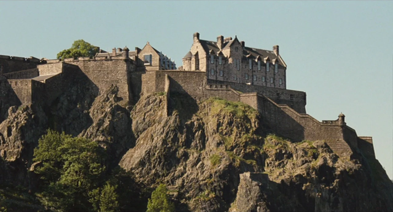 The Angel’s Share (2012) movie still: establishing — A historic stone fortress sits atop a jagged, steep volcanic rock cliff face. Defensive walls…