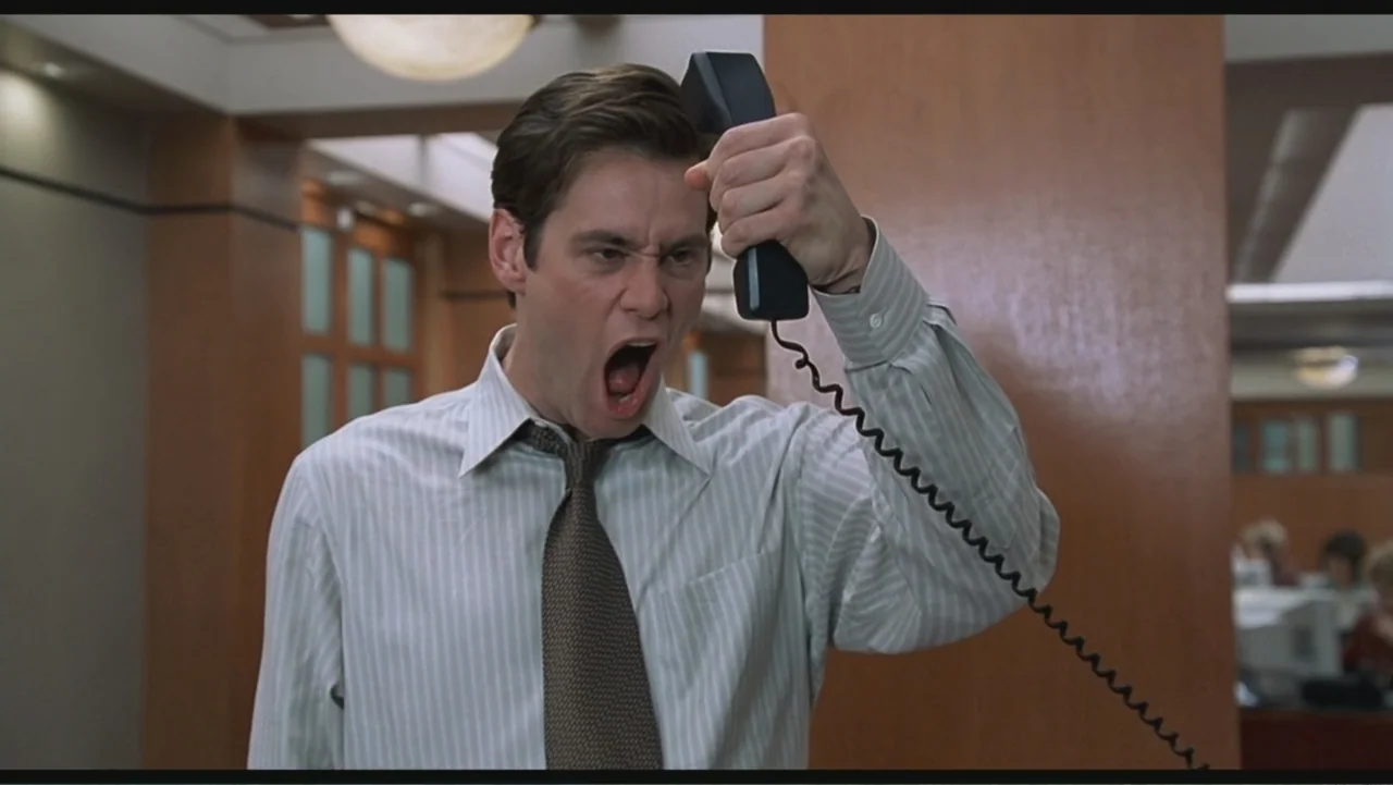 Liar Liar (1997) movie still: medium — An office environment with wood-paneled walls and muted professional lighting. A man stands in the foreground…
