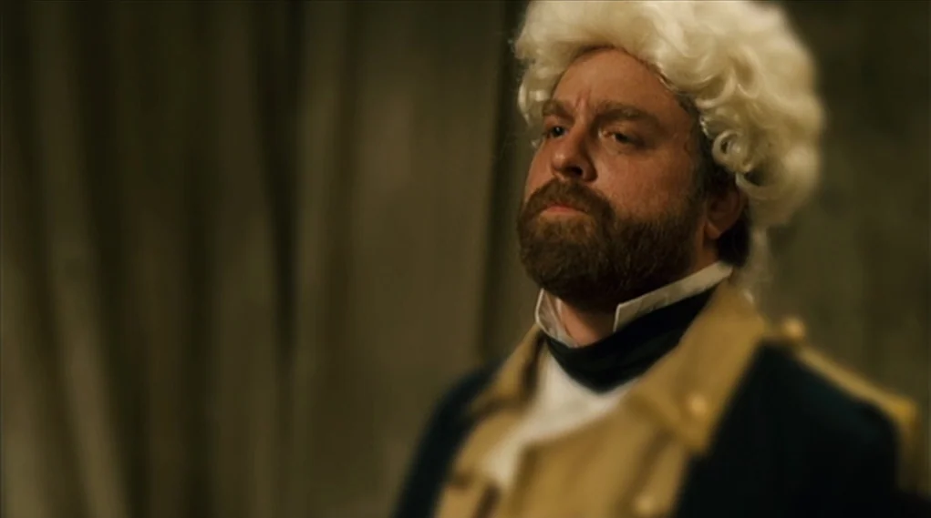 Visioneers (2008) movie still: medium — A man stands indoors wearing a colonial wig and 18th-century military uniform. He stares forward with an…