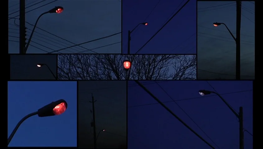 The Tracey Fragments (2007) movie still: establishing — A collage of multiple viewpoints showing streetlamps against a dark blue evening sky. Power…