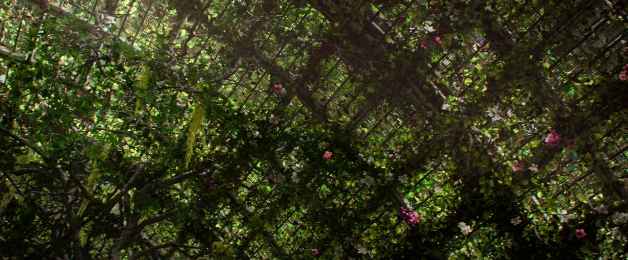 Bird Box (2018) movie still: establishing — A wooden lattice structure is heavily overgrown with tangled vines and small colorful flowers. The…