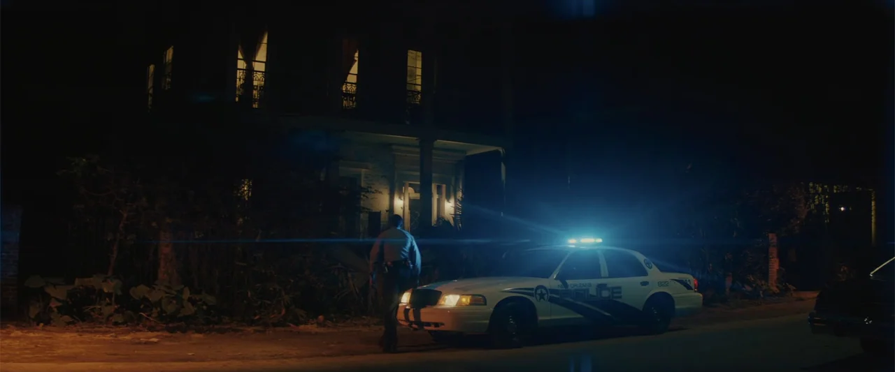 Queen & Slim (2019) movie still: wide — A dark suburban street at night features a New Orleans police vehicle parked in front of a colonial-style…