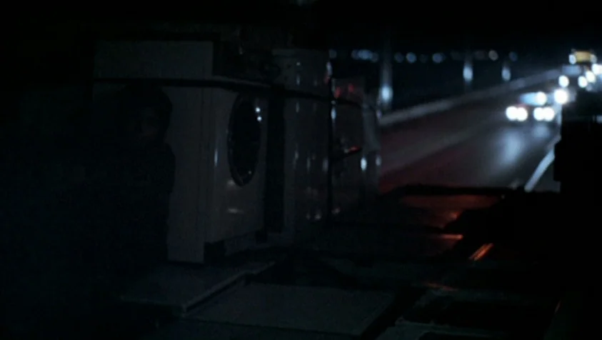 71 Fragments of a Chronology of Chance (1994) movie still: medium — A person sits in the dark bed of a moving truck at night. Distant car lights…