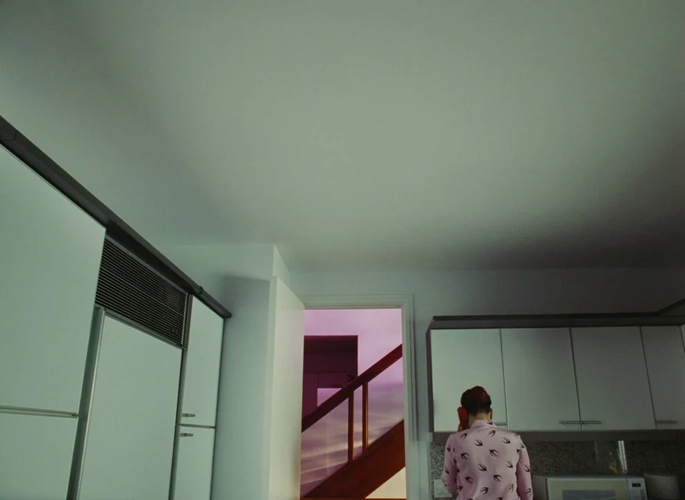 Laurence Anyways (2012) movie still: wide — A modern kitchen with white cabinetry occupies the lower foreground of the frame. A doorway in the…