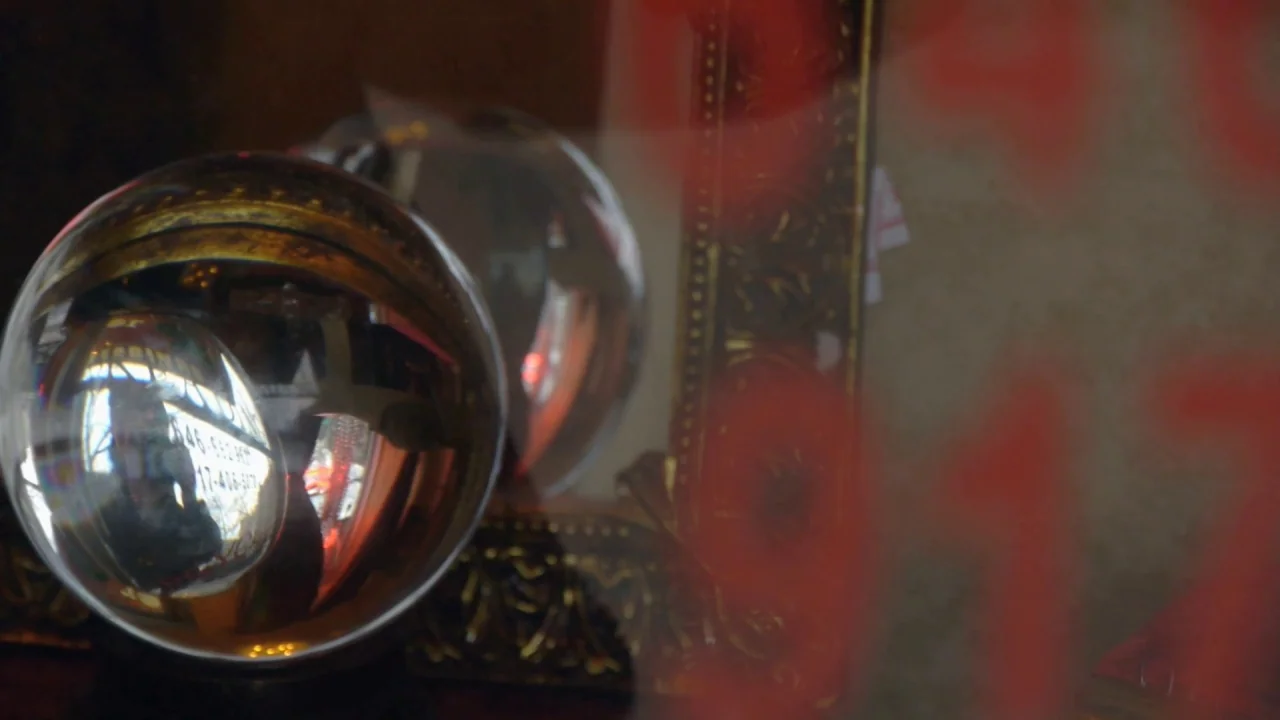 Counting (2015) movie still: closeup — A glass display window showcases decorative objects including a large reflective sphere. Bold red numbers are…