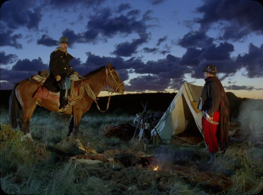 Jauja (2014) movie still: wide — A grassy open plain during dusk features a small cloth tent and campfire. Two men in historical cavalry uniforms…
