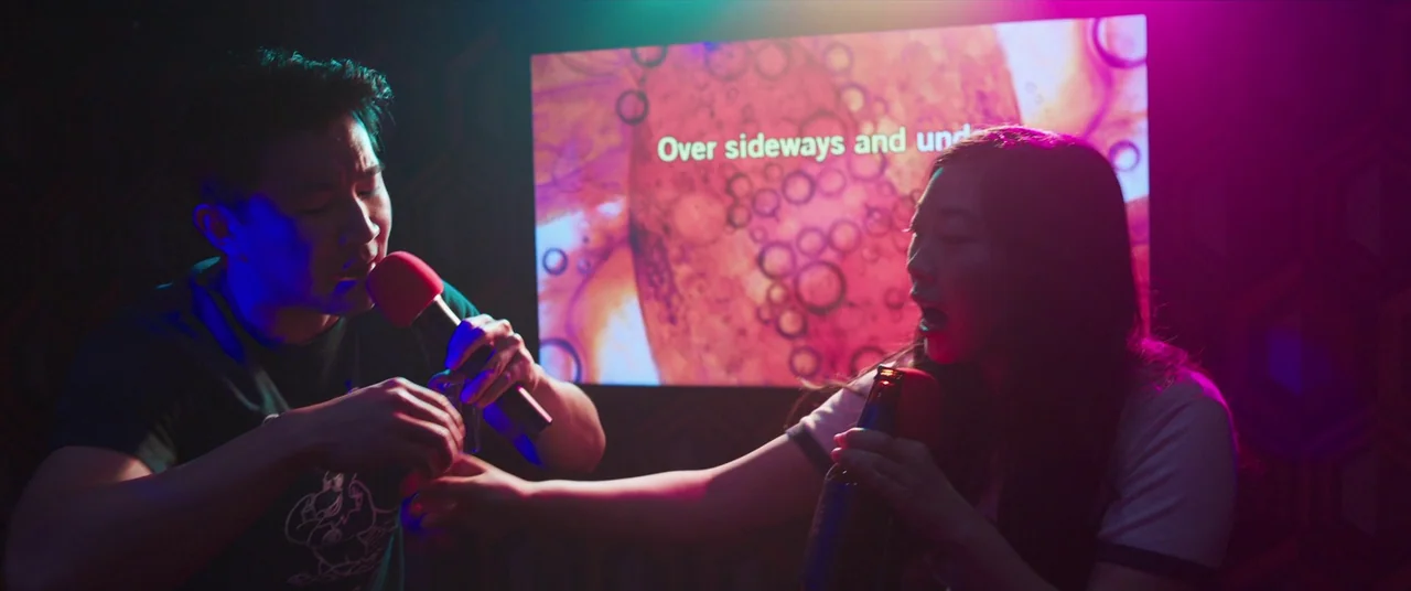 Shang-Chi and the Legend of the Ten Rings (2021) movie still: medium — A small karaoke booth interior features dark walls and a bright television…