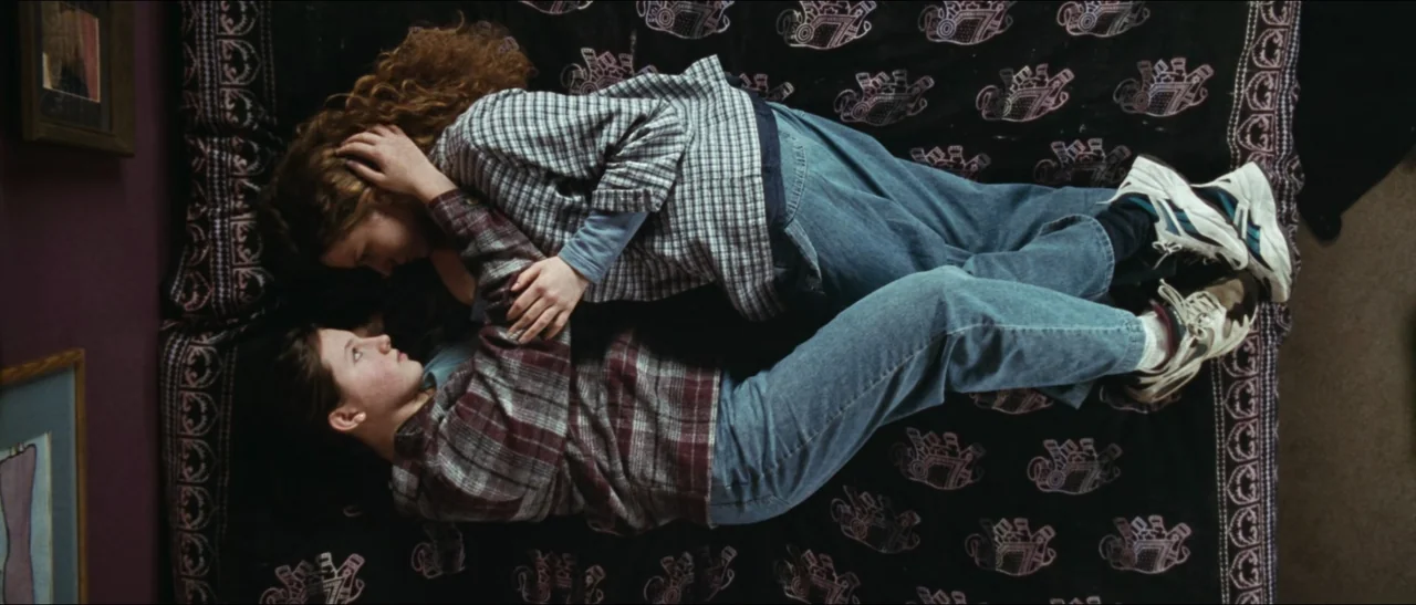 Election (1999) movie still: fullbody — Two individuals lie on a black bedspread patterned with pink elephant designs. They are positioned…