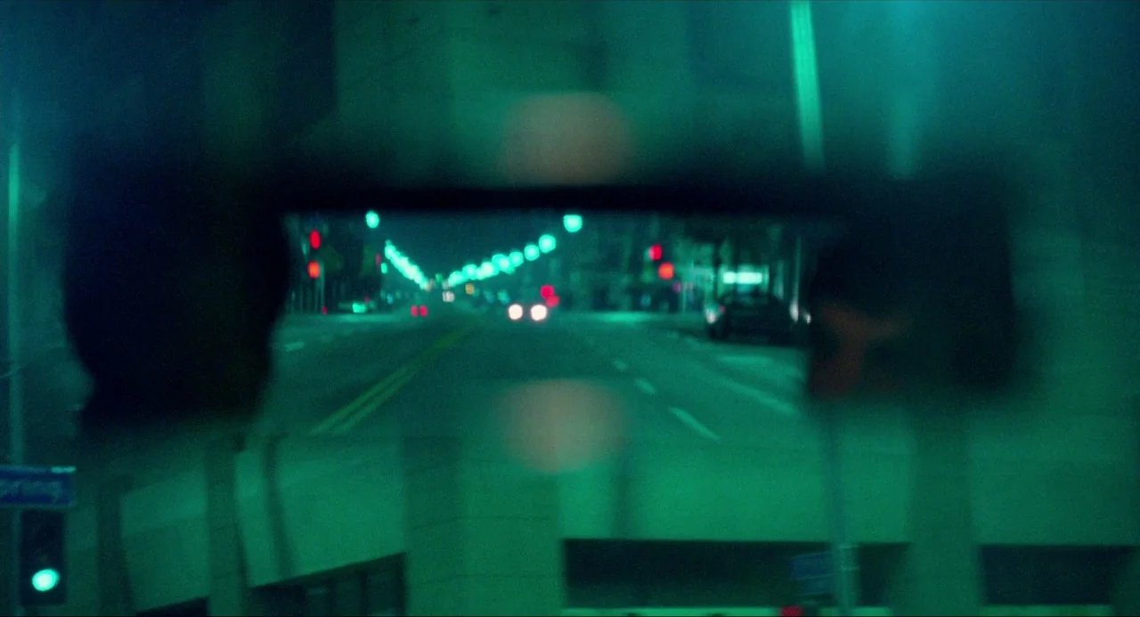 The Driver (1978) movie still: closeup — A view through a car rear-view mirror showing a dark, empty city street at night. The reflection shows the…
