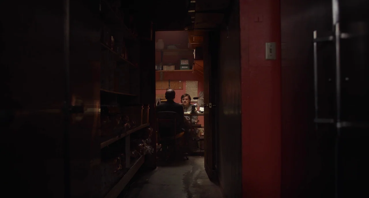An Evening With Beverly Luff Linn (2018) movie still: wide — A dark hallway leads into a cramped back room with red-painted walls and shelving…