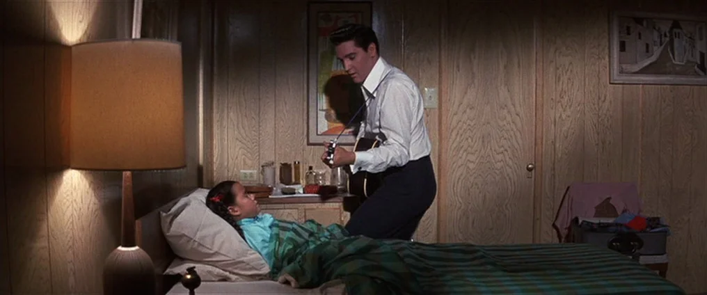 It Happened At The World’s Fair (1963) movie still: medium — A motel room features wood-paneled walls and basic mid-century furnishings. A man…
