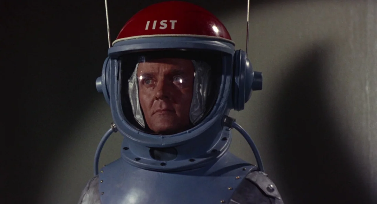 Queen of Blood (1966) movie still: closeup — A dimly lit room serves as the setting for this close-up shot. An astronaut with a red helmet featuring…