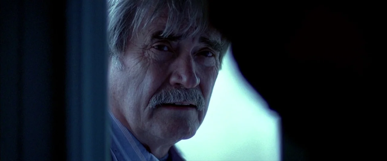 Ballast (2008) movie still: closeup — An elderly man peers through a shadowed doorway with light illuminating his face. He stands partially obscured…