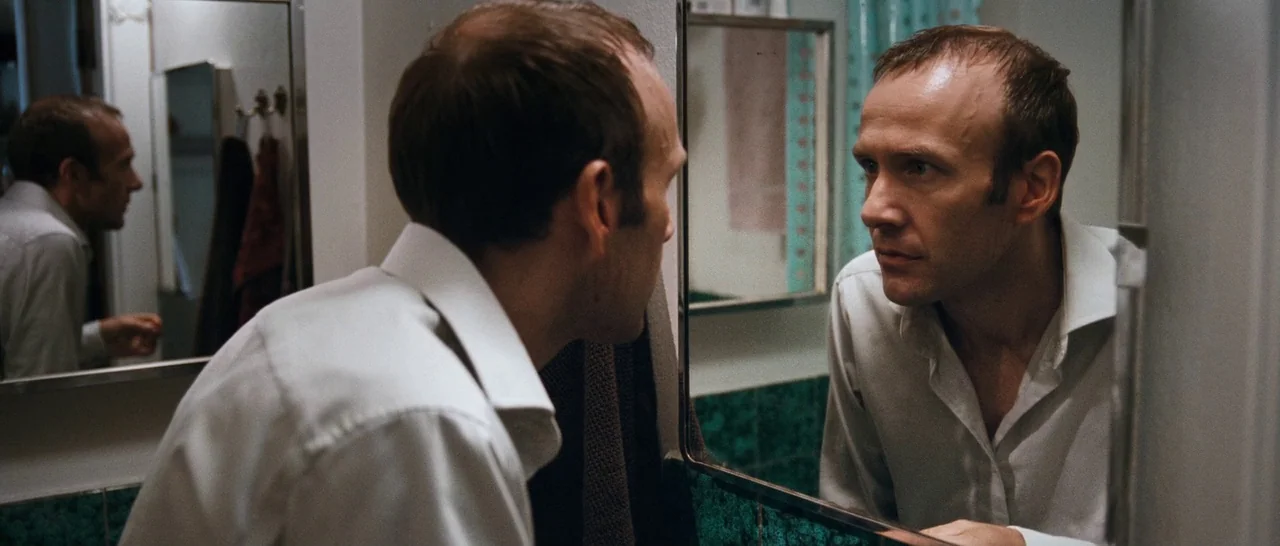 Sound of Noise (2010) movie still: medium — A man stands in a small tiled bathroom with green decorative accents. He observes his reflection in a…