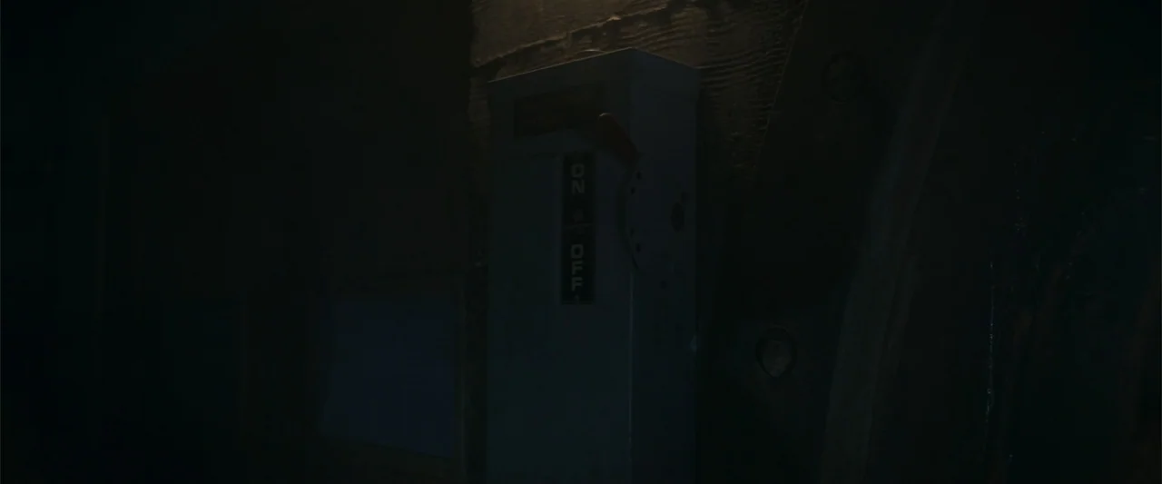 A Christmas Mystery (2022) movie still: closeup — A metal industrial electrical switchbox is mounted to a vertical textured wooden wall. The toggle…
