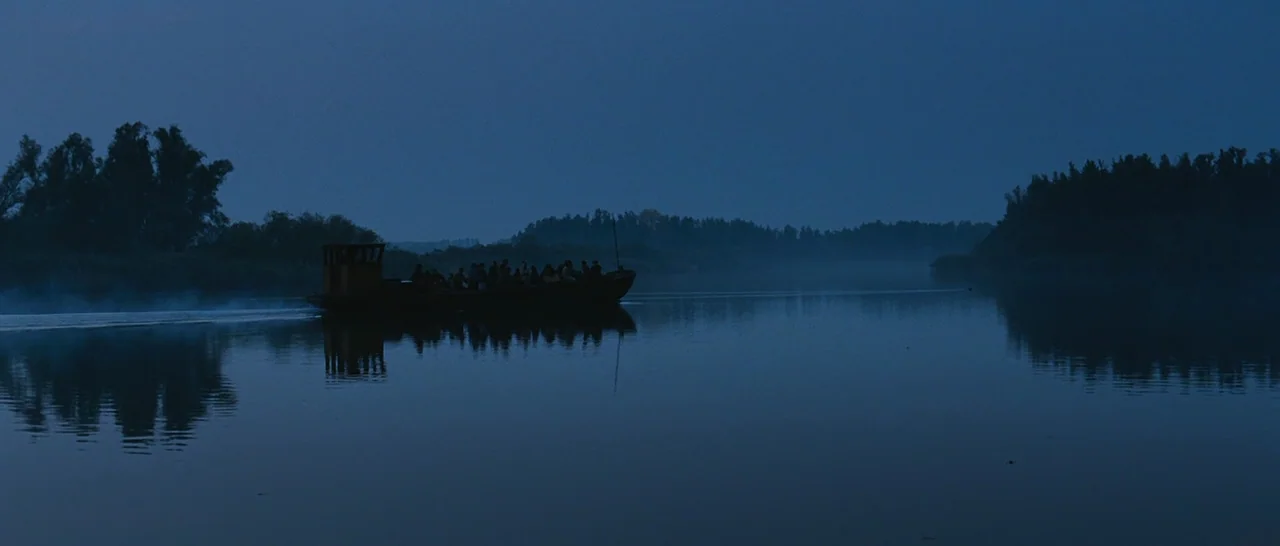 Black Book (2006) movie still: wide — A dark wooden boat moves across a wide river at early dawn. Thin mist clings to the water surface near the…