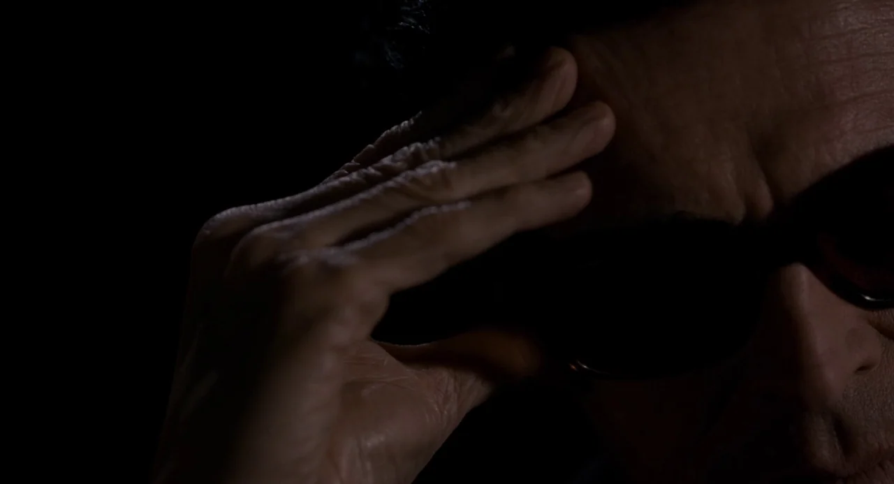 Pasolini (2014) movie still: closeup — A dark, undifferentiated interior space with heavy shadows covering most of the frame. A man touches his…