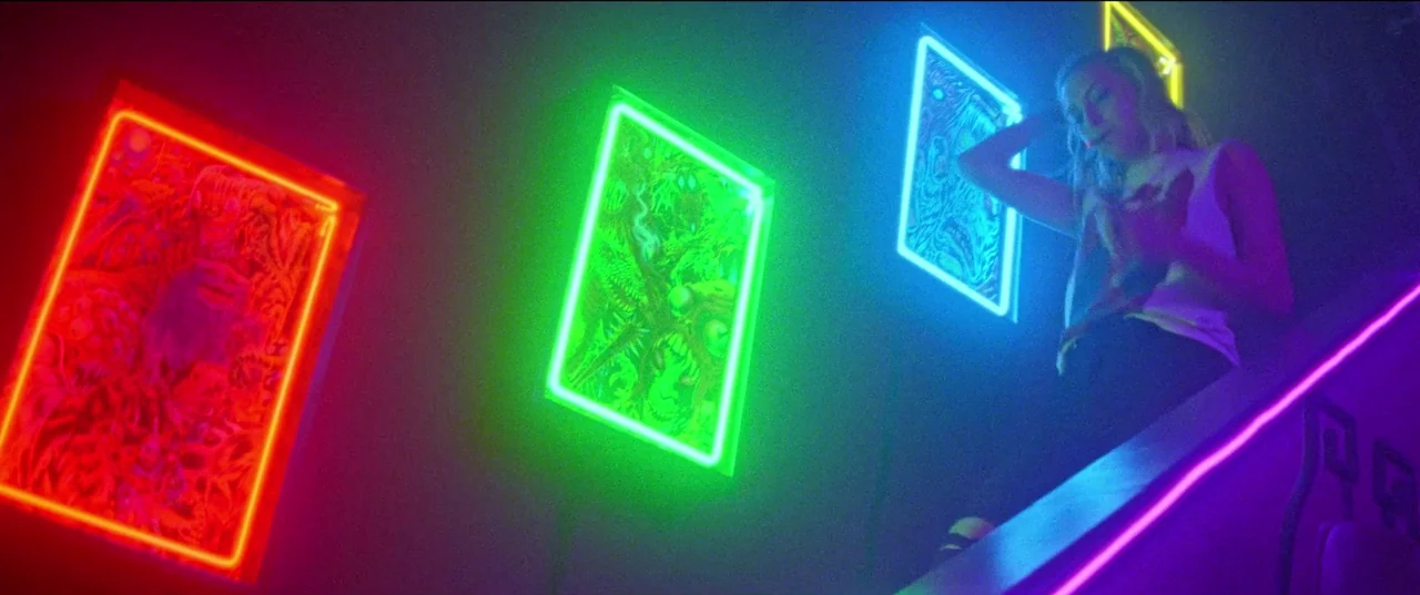 Christmas Bloody Christmas (2022) movie still: wide — A dimly lit staircase features vibrant neon-rimmed posters hung on a dark wall. A young blonde…