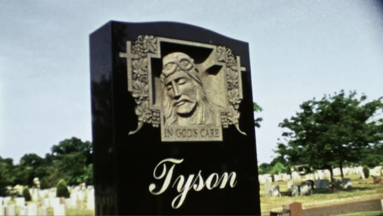 Mike Tyson: Undisputed Truth (2013) movie still: closeup — A polished black granite tombstone features a carved relief of a face. The headstone…