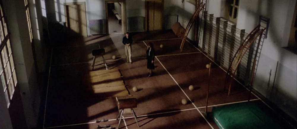 Deep Red (1975) movie still: wide — A high-angle view of an empty gymnasium featuring athletic equipment including vaults and wall bars. A man and a…
