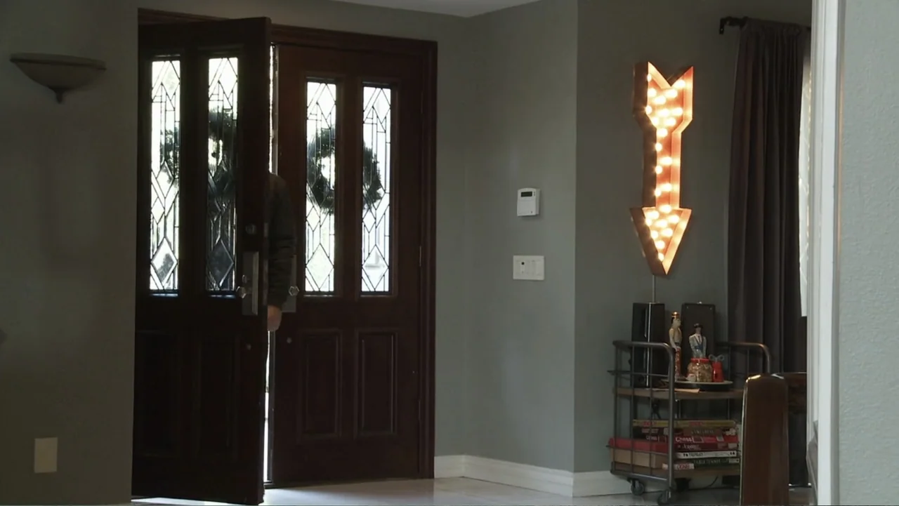 Paranormal Activity: The Ghost Dimension (2015) movie still: medium — A residential foyer with grey walls features a large dark wood front door. A…