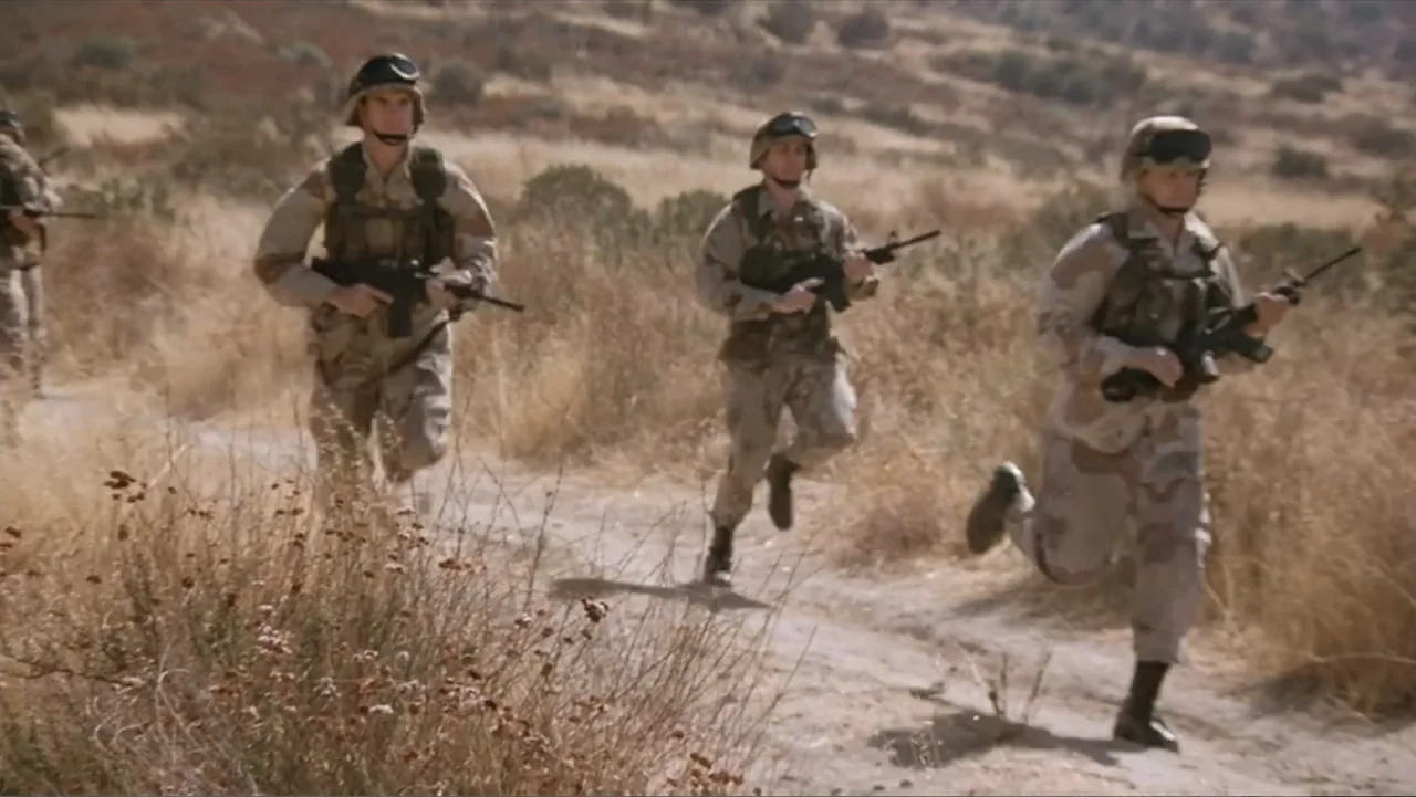 Crisis Point (2012) movie still: fullbody — A group of soldiers in desert camouflage run across a dry, dusty landscape. The soldiers carry rifles…