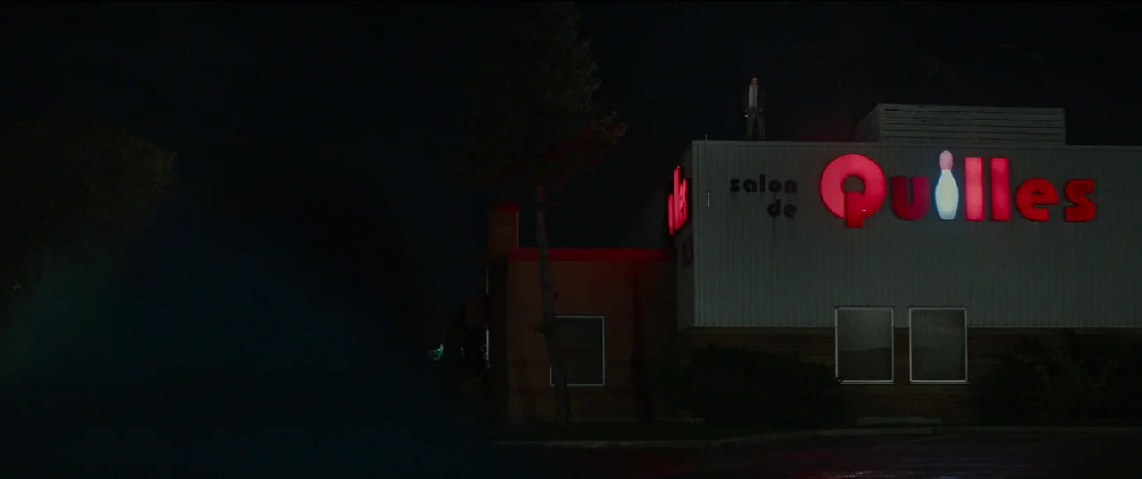 Humanist Vampire Seeking Consenting Suicidal Person (2023) movie still: wide — A single-story building at night features a glowing red neon sign…