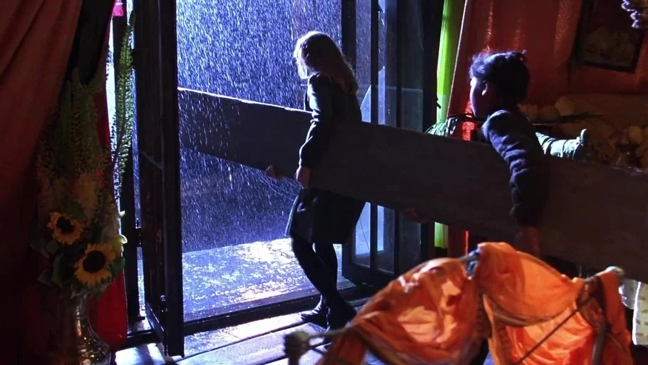 A Little Princess (1995) movie still: medium — An interior room opens to a rainy night outside through a doorway. Two young people work together to…