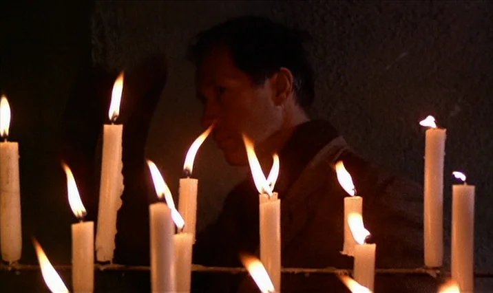 The Serpent’s Egg (1977) movie still: medium — A dimly lit interior space with numerous lit white candles arranged in the foreground. A man stands…