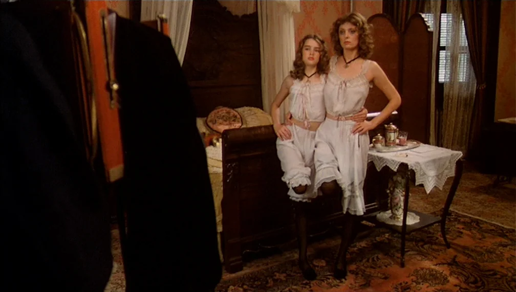 Pretty Baby (1978) movie still: fullbody — A turn-of-the-century bedroom features patterned wallpaper, a wooden bed, and a small lace-covered table.…