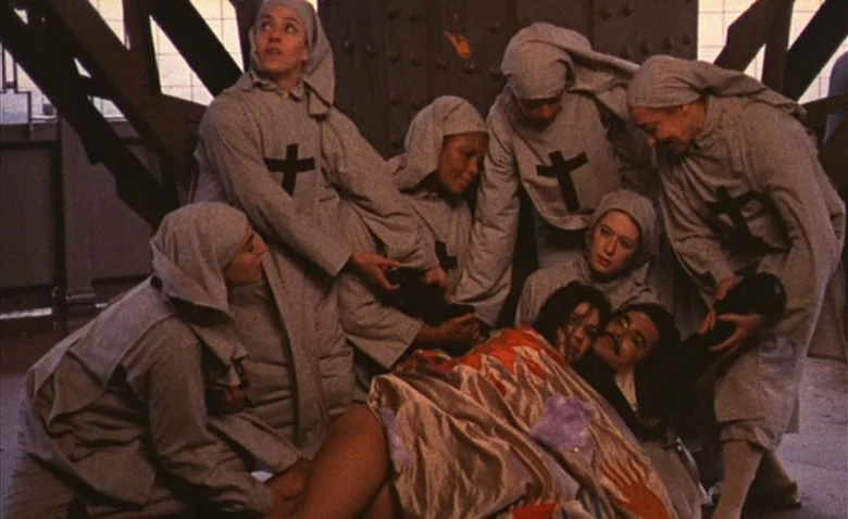 Sweet Movie (1974) movie still: medium — Several women wearing grey religious habits surround two people lying on the ground. The background…