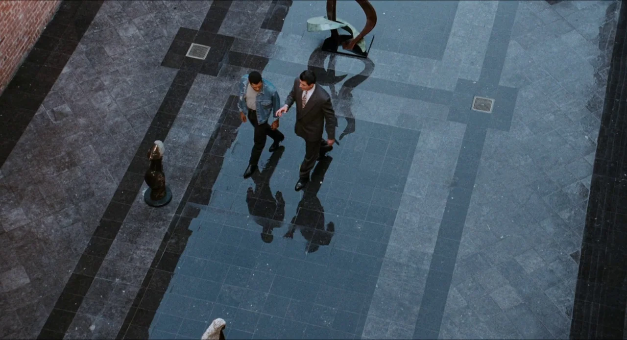Deep Cover (1992) movie still: wide — A spacious atrium with polished grey stone tile floors and brick accents. Two men walk together across the…