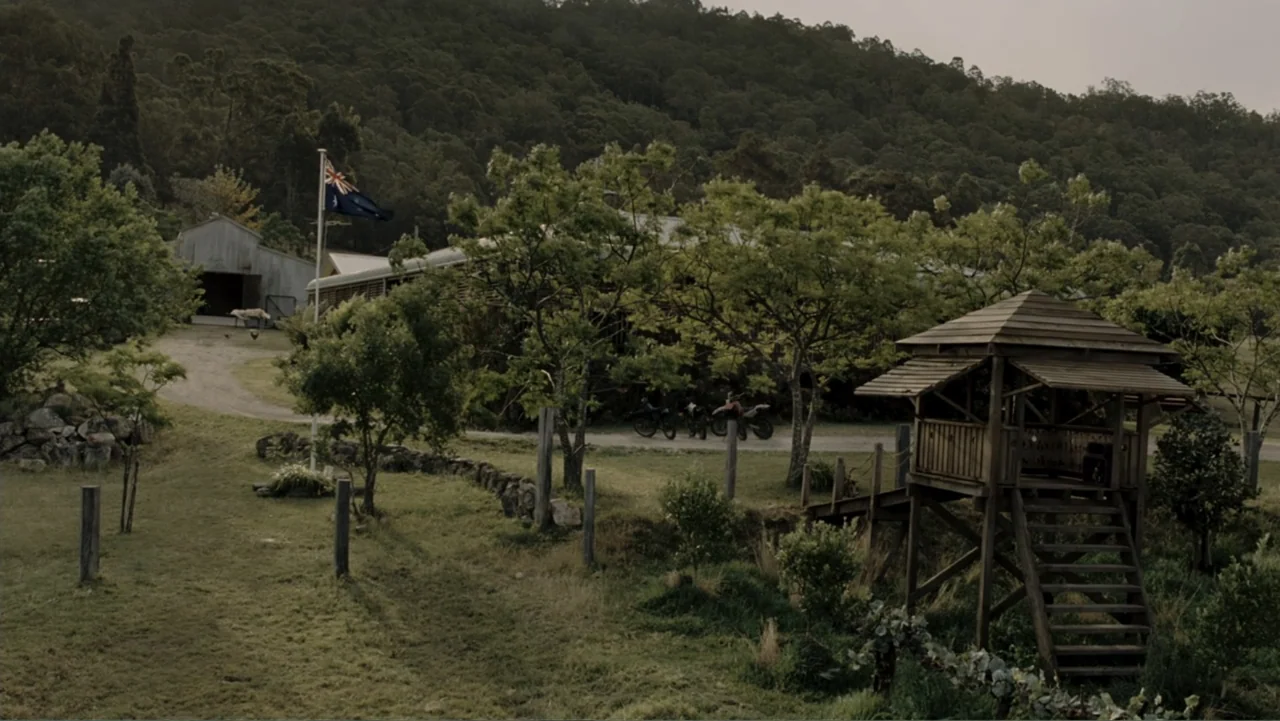 Tomorrow, When the War Began (2010) movie still: wide — A rural property features a wooden lookout tower and a metal-sided barn backdrop. Green…