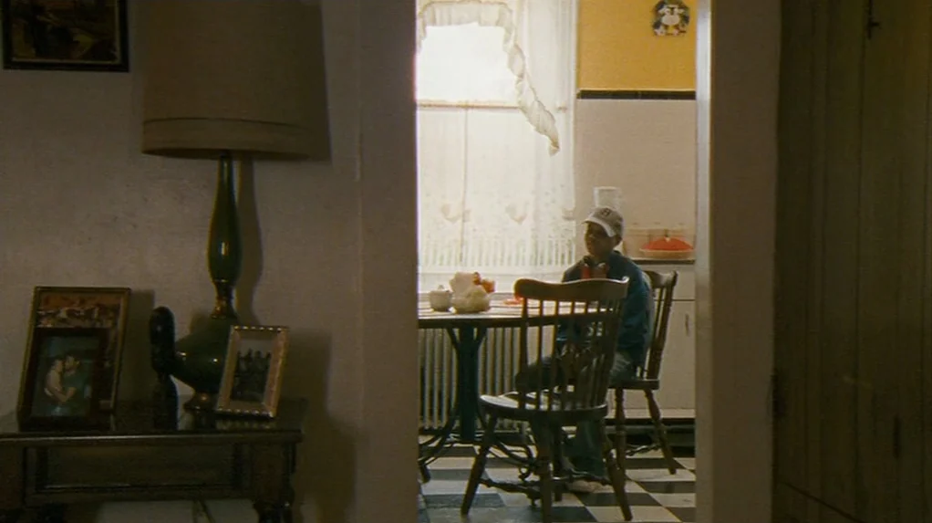 Half Nelson (2006) movie still: wide — A view through a doorway into a home dining area with black and white tiles. A young man sits at a small…