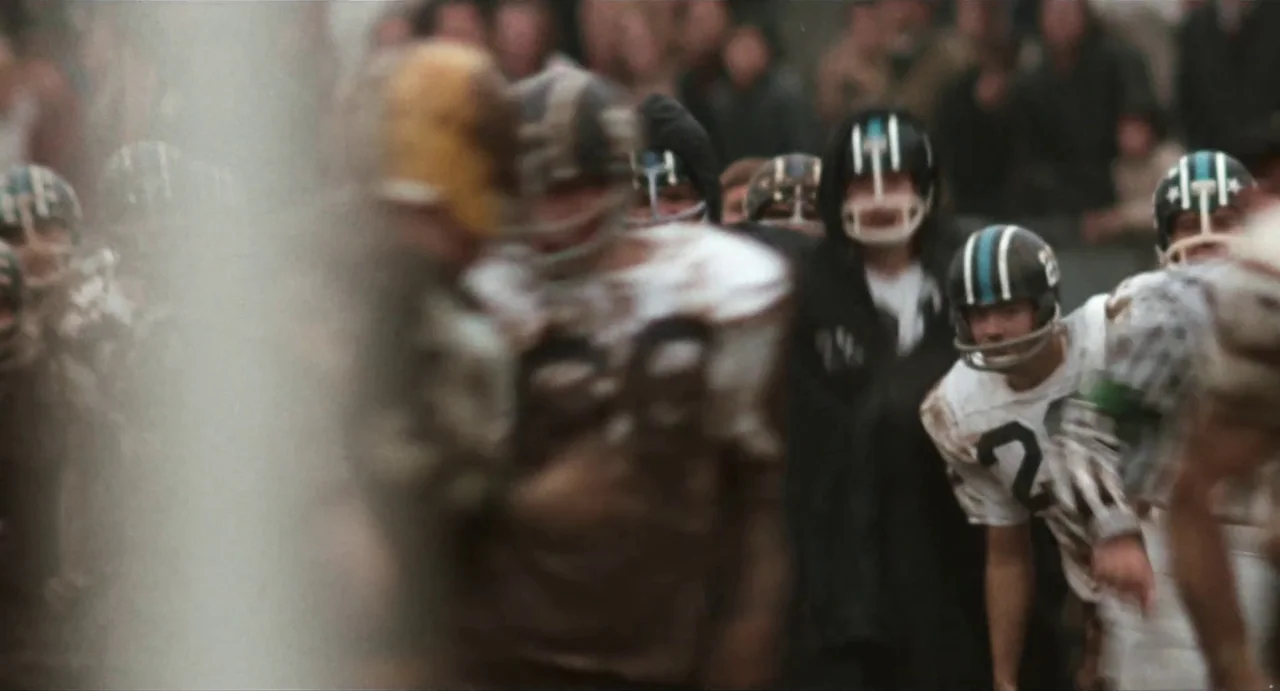 The Rain People (1969) movie still: medium — A football field filled with players wearing vintage jerseys and protective helmets. The players…